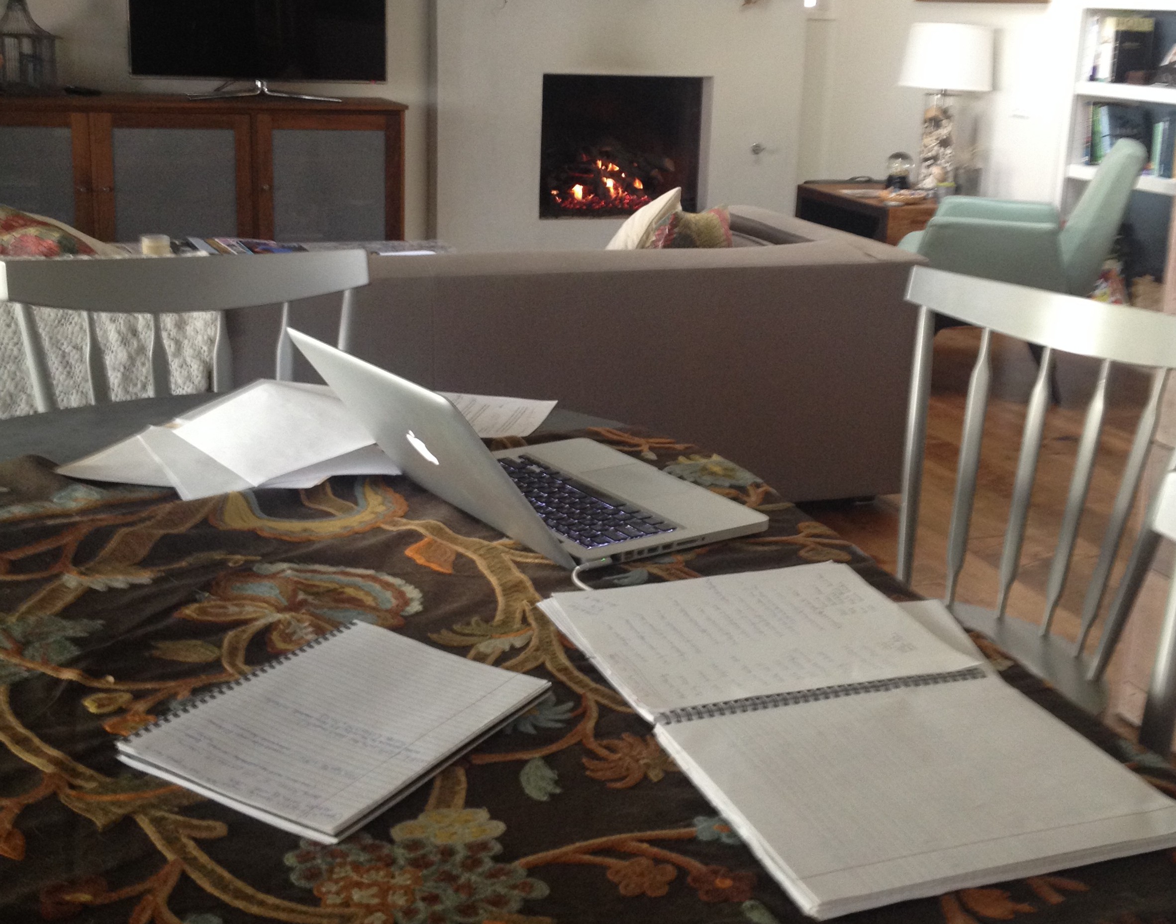 Laptop and notes at table in front of lit fireplace.