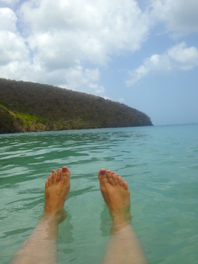 A pair of tanned feet floating in the blue-green waters of the Caribbean.