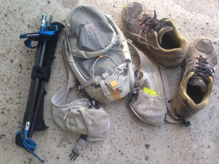 Folded trekking poles are next to backpack and shoes for size comparison.
