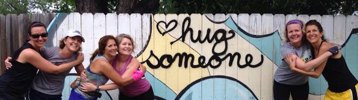 Women runners hug in front of graffiti that says "Hug Someone."