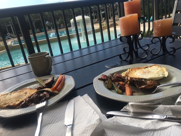 Two plates of breakfast on outdoor patio overlooking pool in Destin.