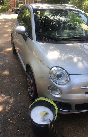 Fiat 500 with bucket full of suds, sponge, and hose near front wheel.