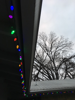 Christmas lights on eaves against a gray sky.